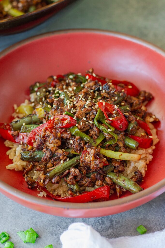 Mongolian tofu stir-fry with crispy grated tofu, green beans, and red chilies served over steamed rice with toasted sesame seeds garnish
