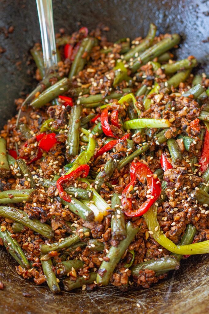 Mongolian tofu stir-fry with crispy grated tofu, green beans, and red chilies garnished with toasted sesame seeds garnish