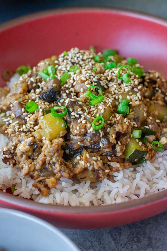 Vegan mushroom tofu stir-fry served over white rice with green onion and toasted sesame seed garnish