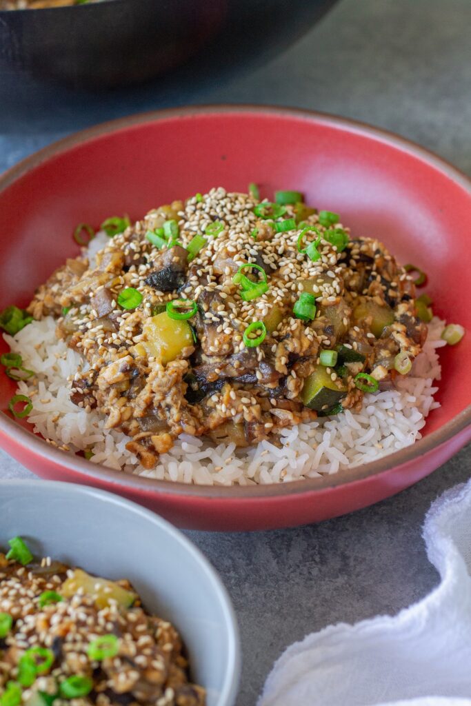 Vegan mushroom tofu stir-fry served over white rice with green onion and toasted sesame seed garnish