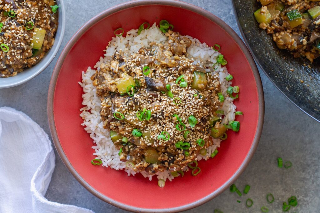 Vegan mushroom tofu stir-fry served over white rice with green onion and toasted sesame seed garnish