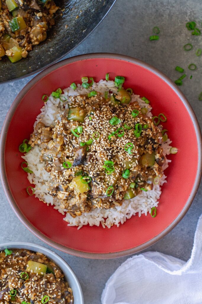 Vegan mushroom tofu stir-fry served over white rice with green onion and toasted sesame seed garnish