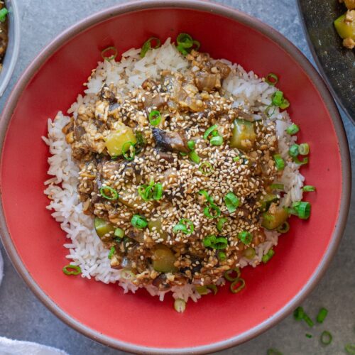 Vegan mushroom tofu stir-fry served over white rice with green onion and toasted sesame seed garnish