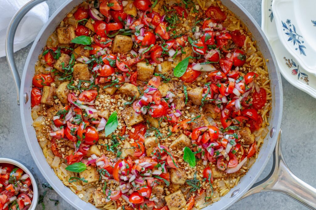 Skillet Bruschetta Tofu and Orzo with juicy tomato topping, garlic breadcrumbs, and sliced basil garnish