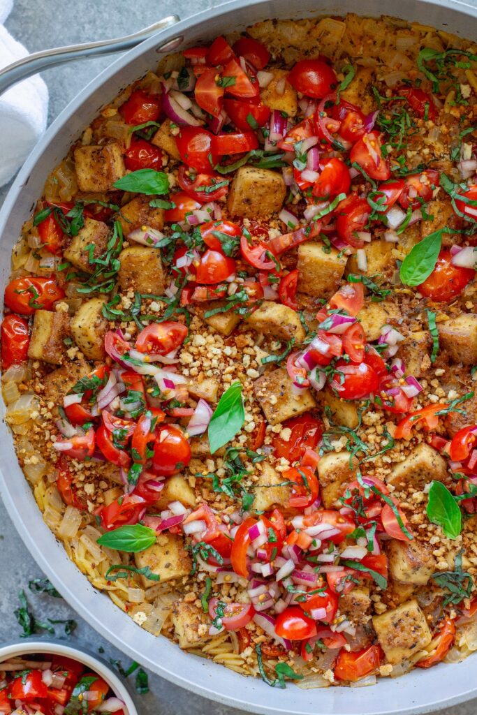 Skillet Bruschetta Tofu and Orzo with juicy tomato topping, garlic breadcrumbs, and sliced basil garnish