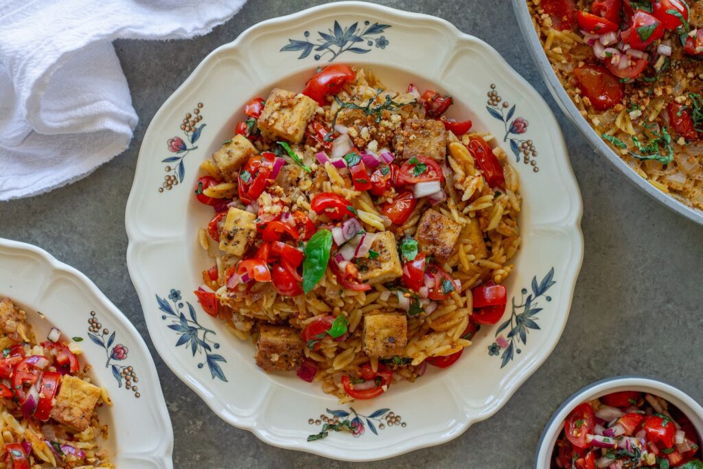 Skillet Bruschetta Tofu and Orzo served on plates with juicy tomato topping, garlic breadcrumbs, and sliced basil garnish