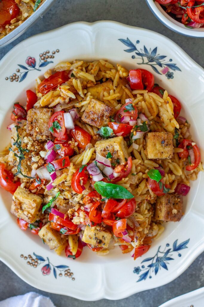 Skillet Bruschetta Tofu and Orzo served on plates with juicy tomato topping, garlic breadcrumbs, and sliced basil garnish