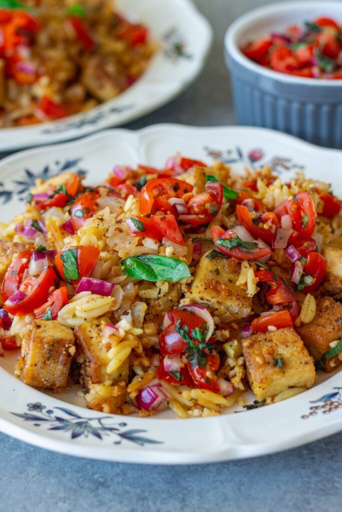 Skillet Bruschetta Tofu and Orzo served on plates with juicy tomato topping, garlic breadcrumbs, and sliced basil garnish