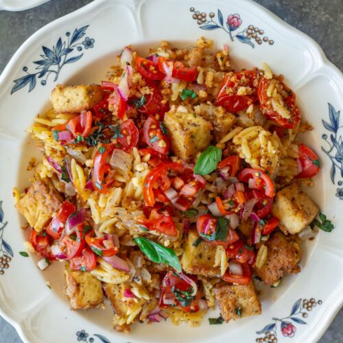 Skillet Bruschetta Tofu and Orzo served on plates with juicy tomato topping, garlic breadcrumbs, and sliced basil garnish