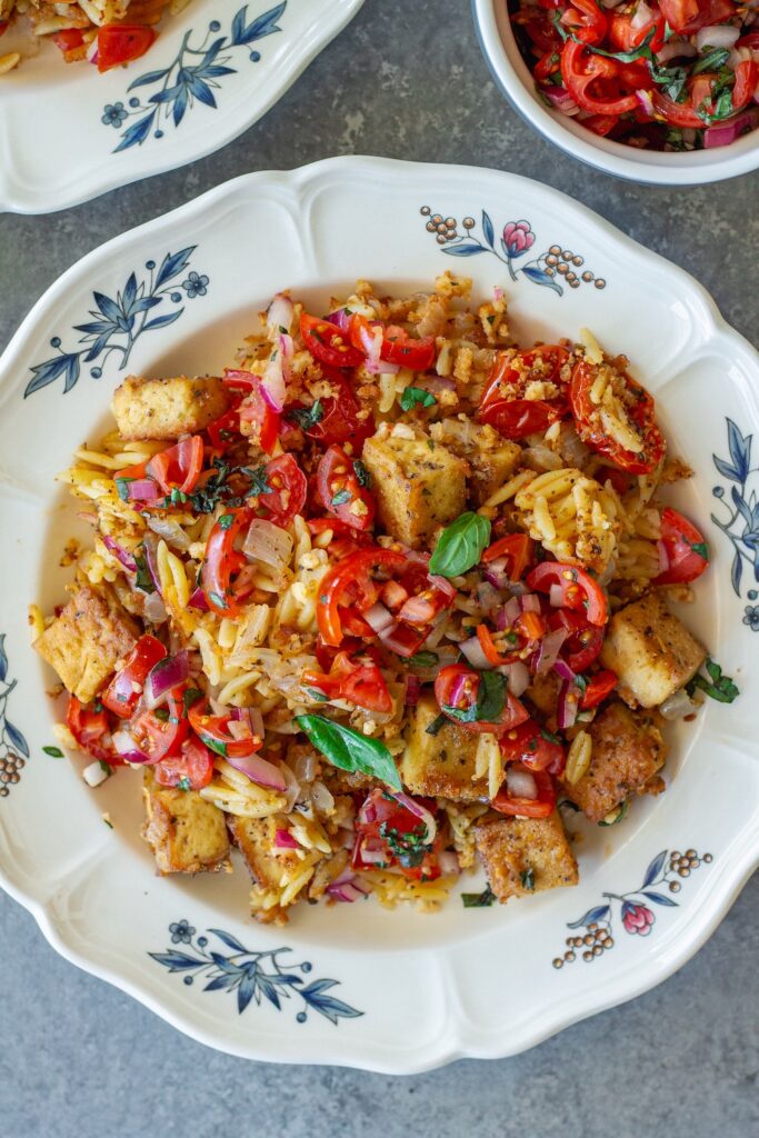Skillet Bruschetta Tofu and Orzo served on plates with juicy tomato topping, garlic breadcrumbs, and sliced basil garnish
