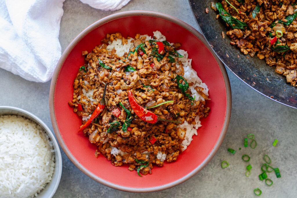 Thai basil tofu stir-fry served over fluffy jasmine rice, garnished with lime wedges and fresh basil sprigs.