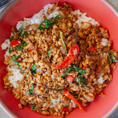 Thai basil tofu stir-fry served over fluffy jasmine rice, garnished with lime wedges and fresh basil sprigs.