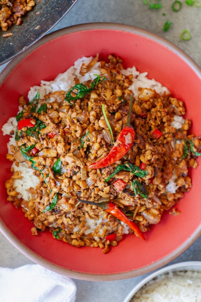 Thai basil tofu stir-fry served over fluffy jasmine rice, garnished with lime wedges and fresh basil sprigs.