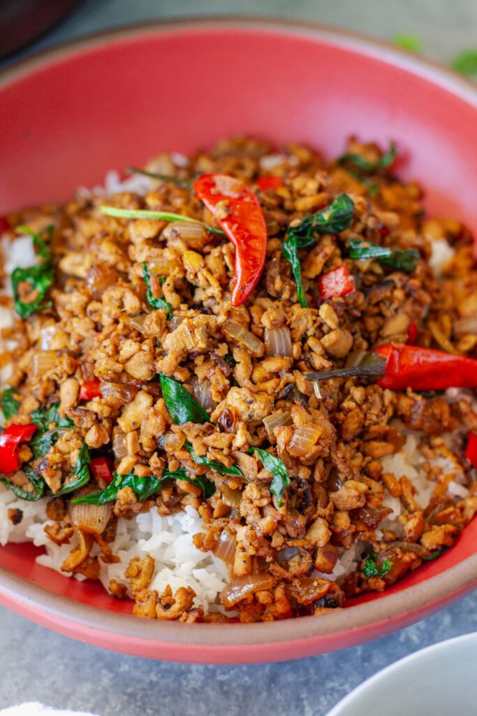Thai basil tofu stir-fry served over fluffy jasmine rice, garnished with lime wedges and fresh basil sprigs.