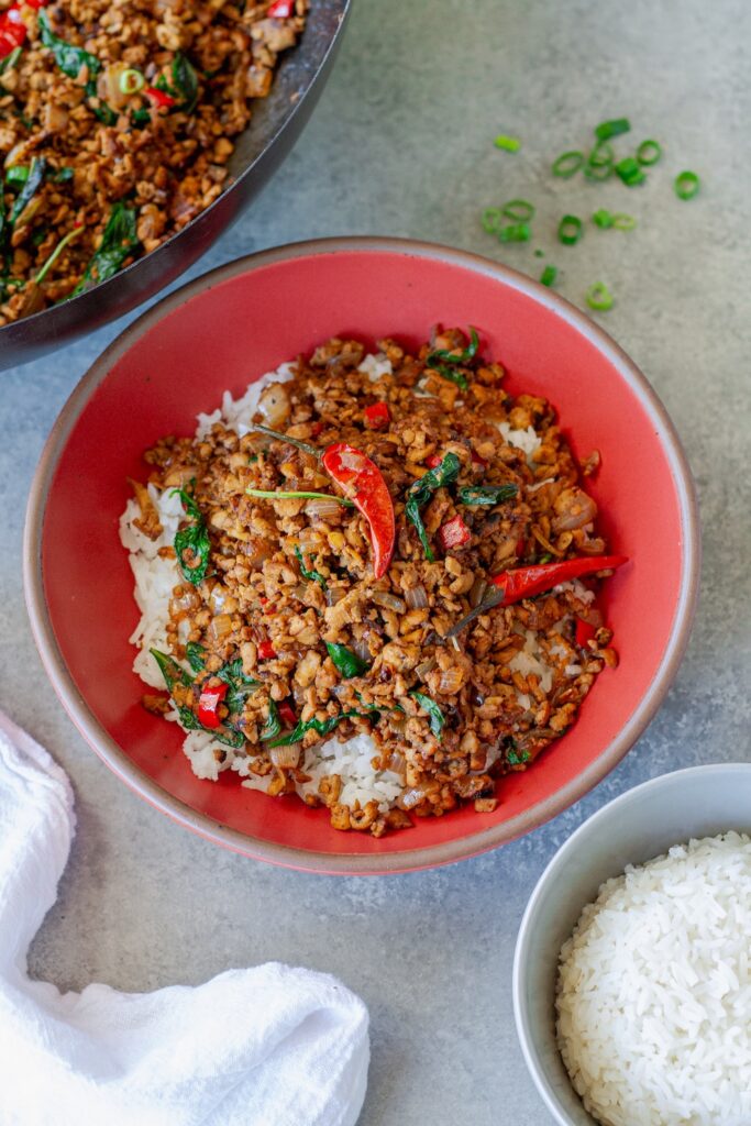 Thai basil tofu stir-fry served over fluffy jasmine rice, garnished with lime wedges and fresh basil sprigs.