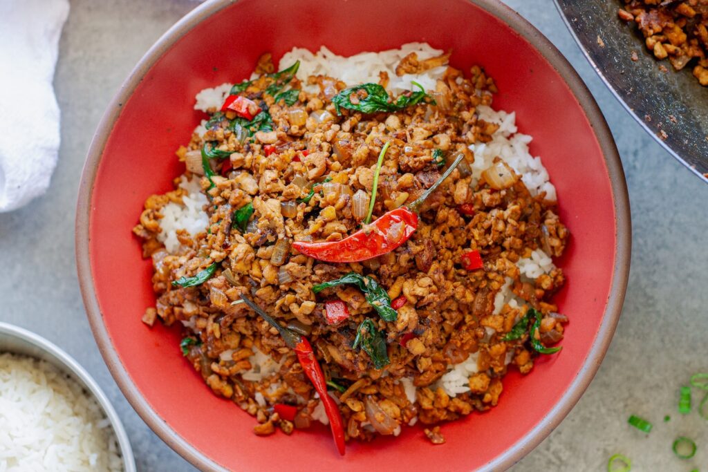 Thai basil tofu stir-fry served over fluffy jasmine rice, garnished with lime wedges and fresh basil sprigs.