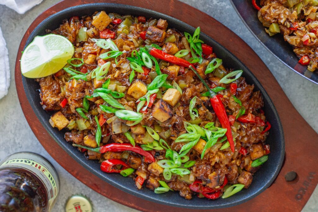 Vegan sisig with crispy tofu and snow mushrooms served on sizzling plate with calamansi wedges