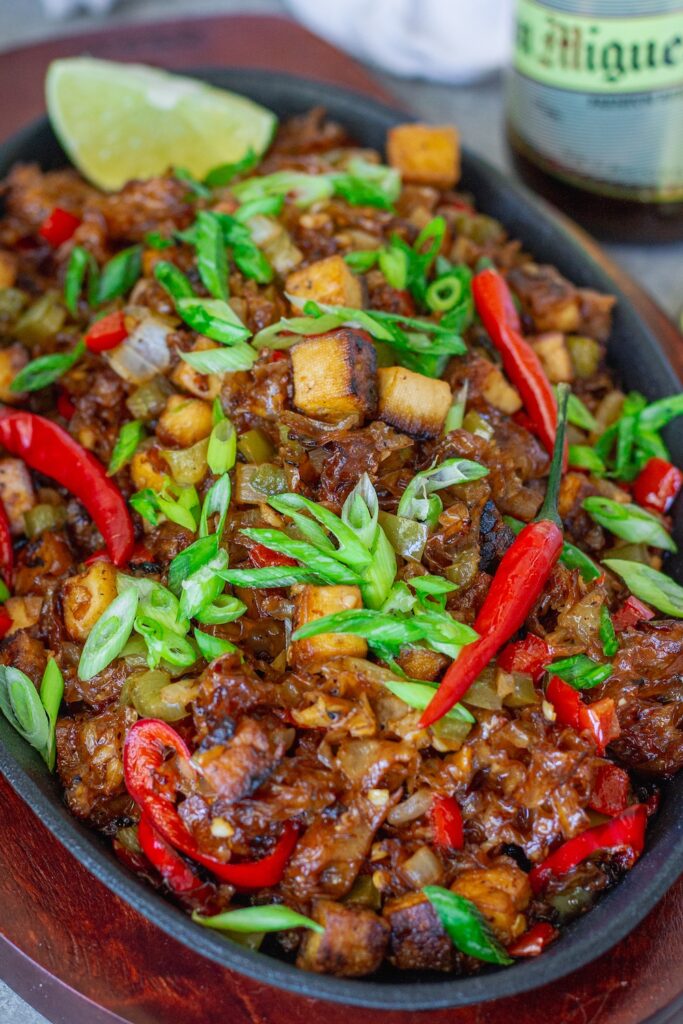 Vegan sisig with crispy tofu and snow mushrooms served on sizzling plate with calamansi wedges