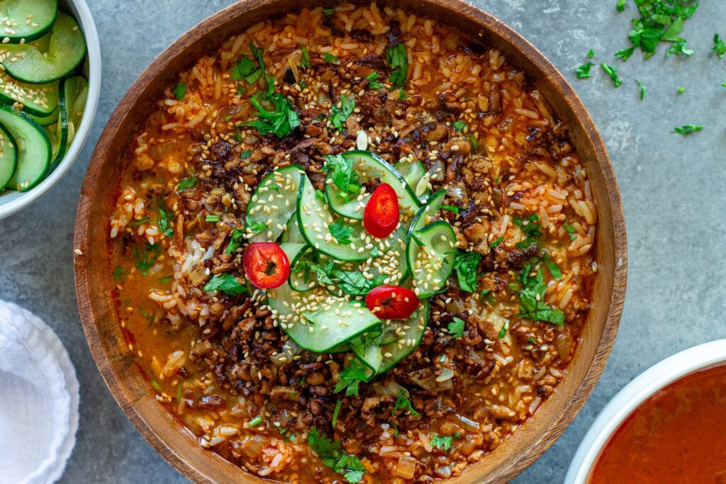 Crispy ginger tofu coconut curry brothy rice in a bowl topped with cucumber salad and sesame seeds. served with a lime wedge on the side.