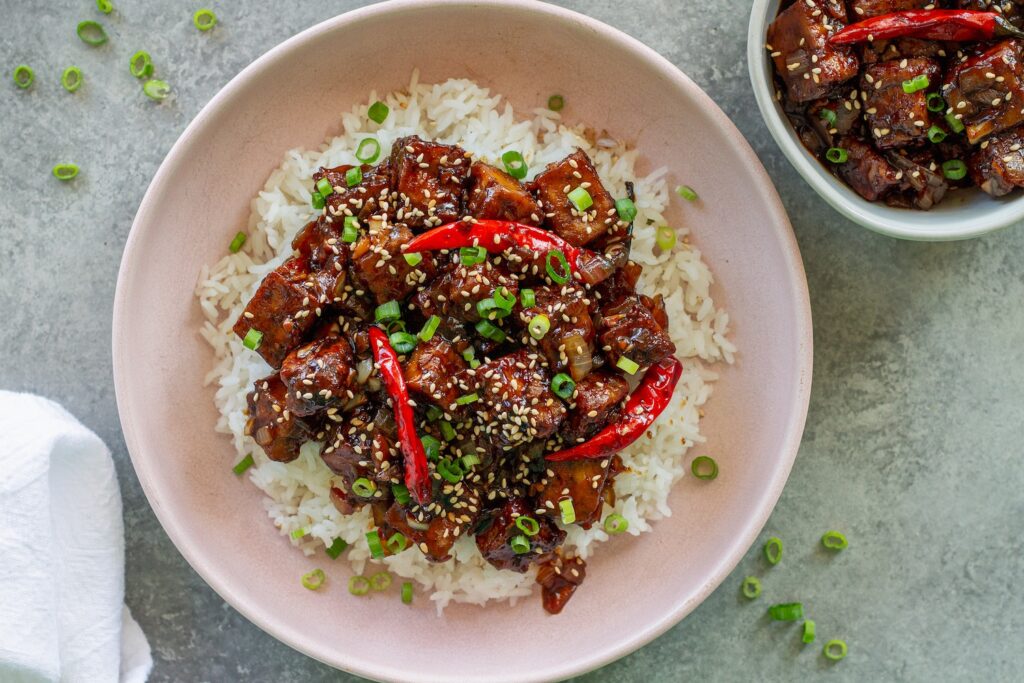 Close-up of finished General Tso's tofu served over rice and garnished with toasted sesame seeds and sliced green onion.