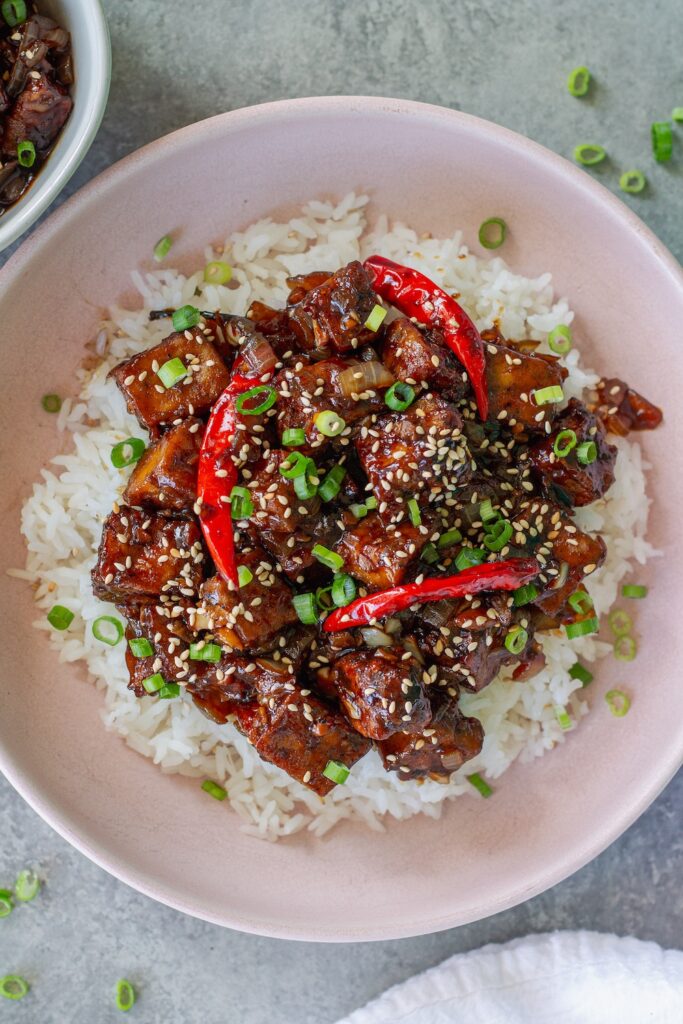Close-up of finished General Tso's tofu served over rice and garnished with toasted sesame seeds and sliced green onion.