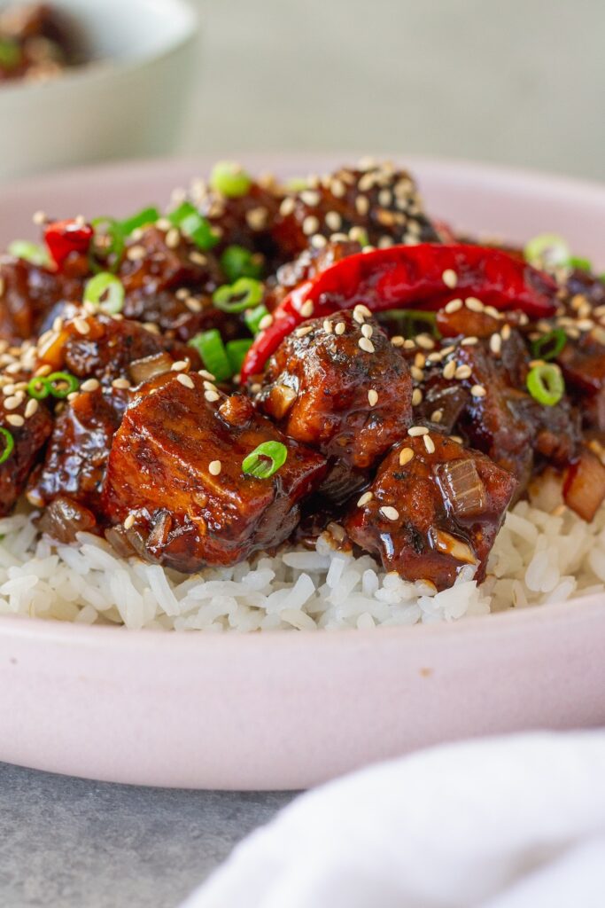 Close-up of finished General Tso's tofu served over rice and garnished with toasted sesame seeds and sliced green onion.