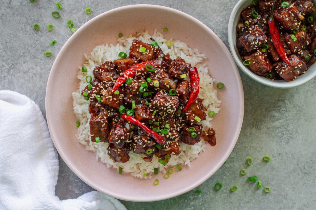 Close-up of finished General Tso's tofu served over rice and garnished with toasted sesame seeds and sliced green onion.