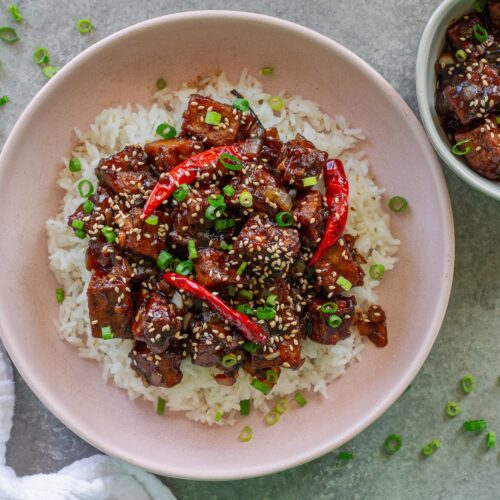 Close-up of finished General Tso's tofu served over rice and garnished with toasted sesame seeds and sliced green onion.