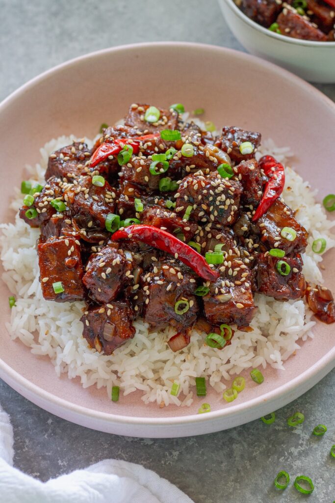 Close-up of finished General Tso's tofu served over rice and garnished with toasted sesame seeds and sliced green onion.