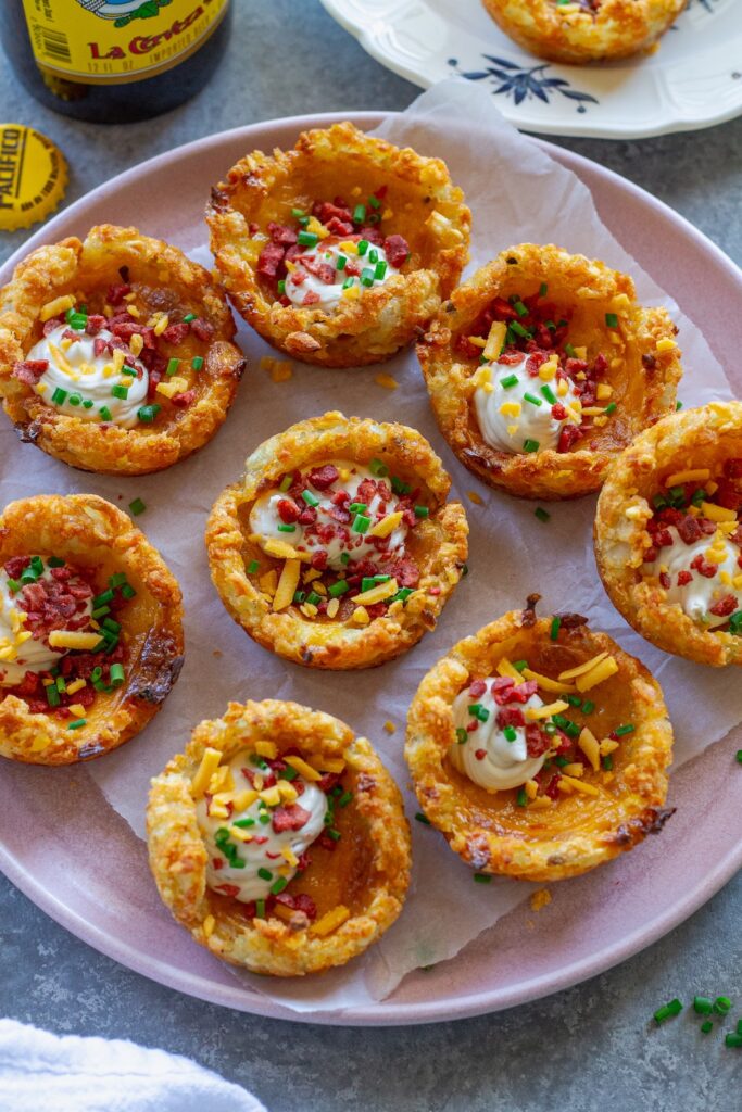 Close-up of loaded tater tot cups with melted cheese, sour cream, vegan bacon bits and chives.