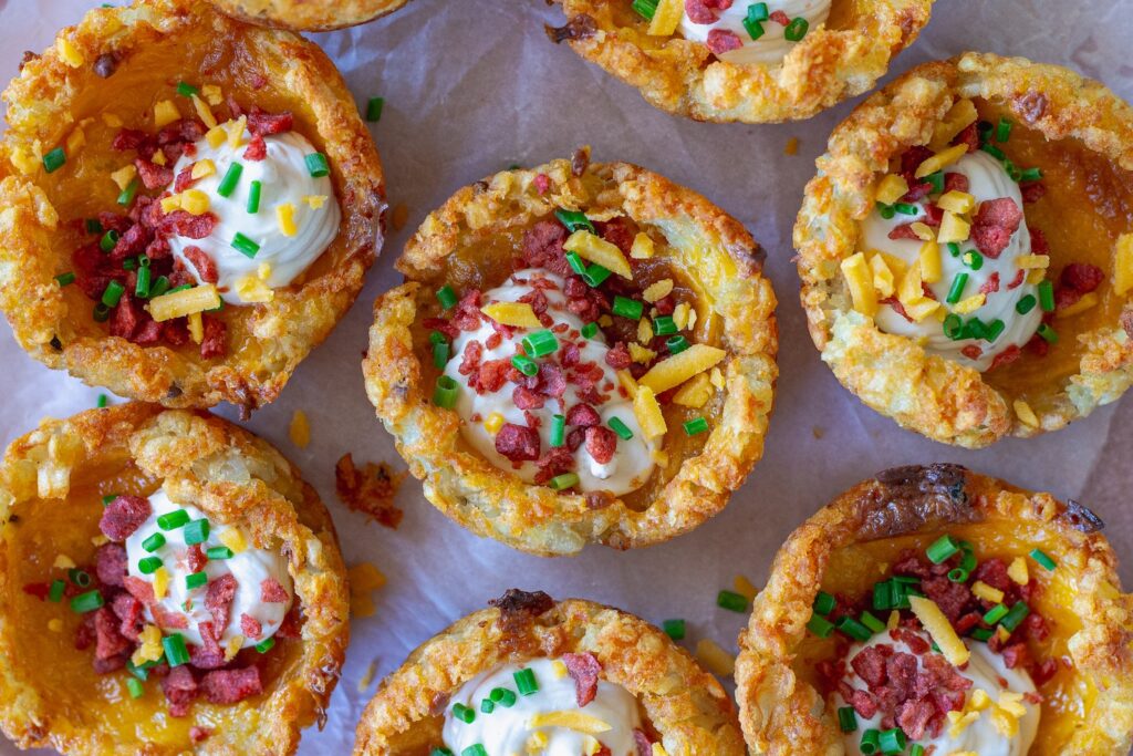 Close-up of loaded tater tot cups with melted cheese, sour cream, vegan bacon bits and chives.