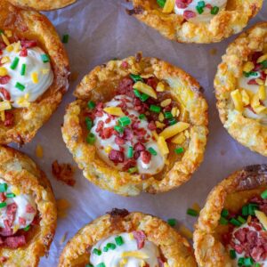 Close-up of loaded tater tot cups with melted cheese, sour cream, vegan bacon bits and chives.