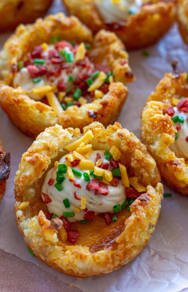 Close-up of loaded tater tot cups with melted cheese, sour cream, vegan bacon bits and chives.