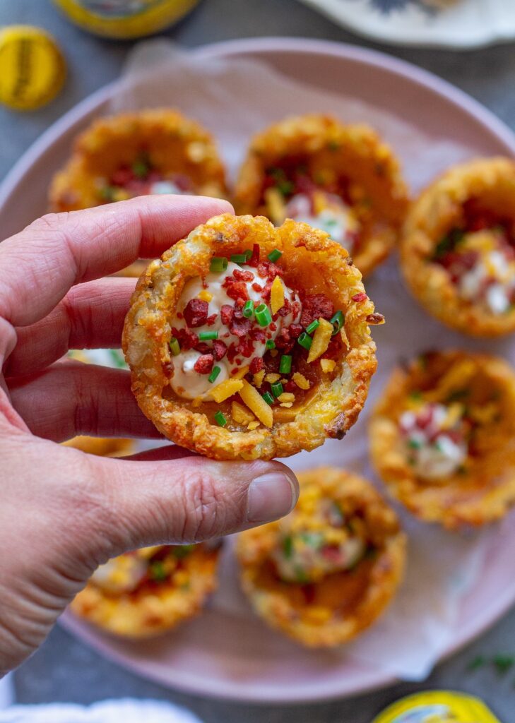 Close-up of loaded tater tot cups with melted cheese, sour cream, vegan bacon bits and chives.