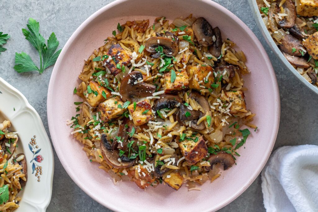 Golden crispy tofu in creamy marsala orzo with mushrooms and fresh parsley garnish.