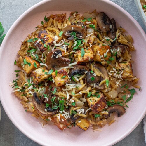 Golden crispy tofu in creamy marsala orzo with mushrooms and fresh parsley garnish.