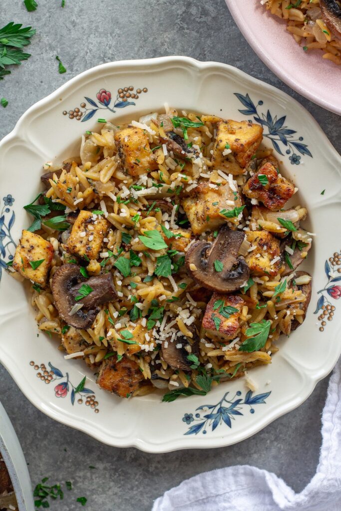 Golden crispy tofu in creamy marsala orzo with mushrooms and fresh parsley garnish.