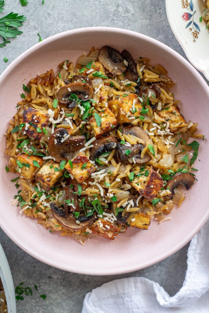 Golden crispy tofu in creamy marsala orzo with mushrooms and fresh parsley garnish.
