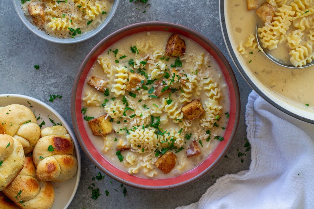 bowl of Vegan Chicken Alfredo Soup with crispy tofu cubes, creamy broth and fresh parsley and parmesan garnish