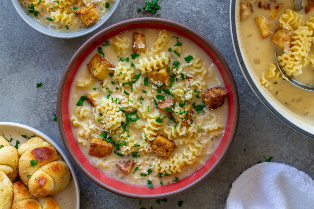 bowl of Vegan Chicken Alfredo Soup with crispy tofu cubes, creamy broth and fresh parsley and parmesan garnish