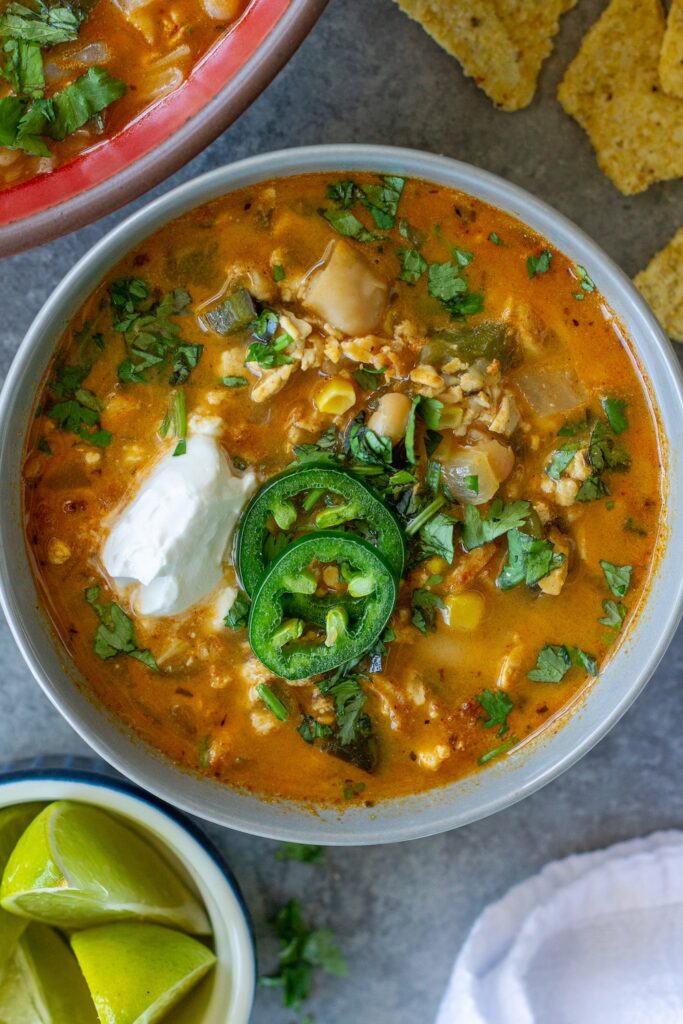 Creamy vegan white chicken chili topped with cheese, sour cream, cilantro, jalapeño, and tortilla chips