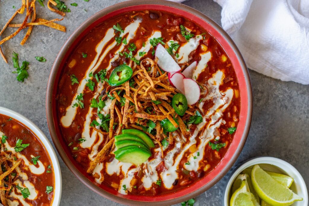 Bowl of vegan chicken enchilada soup topped with cilantro, thinly sliced radish, jalapeño, avocado and tortilla strips
