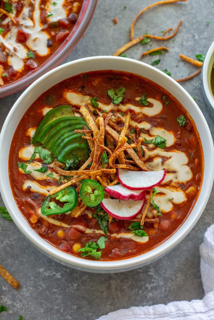 Bowl of vegan chicken enchilada soup topped with cilantro, thinly sliced radish, jalapeño, avocado and tortilla strips