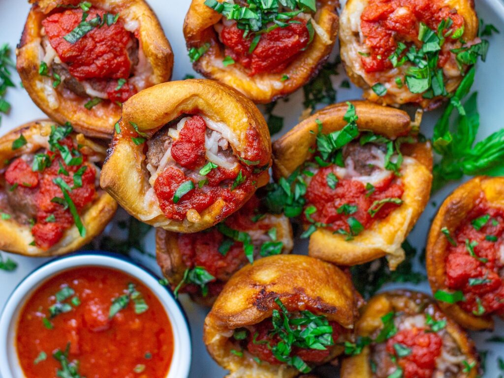 Golden brown vegan meatball sub bites with fresh basil and parmesan garnish and small bowl of marinara for dipping