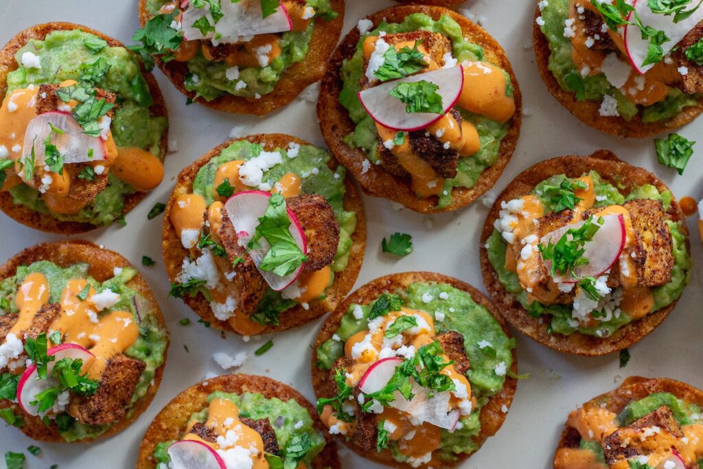 Bite-sized vegan tostadas with guacamole, crispy tofu, chipotle sour cream, and cilantro garnish