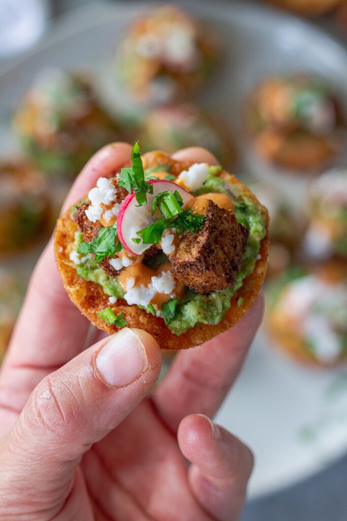 Bite-sized vegan tostadas with guacamole, crispy tofu, chipotle sour cream, and cilantro garnish