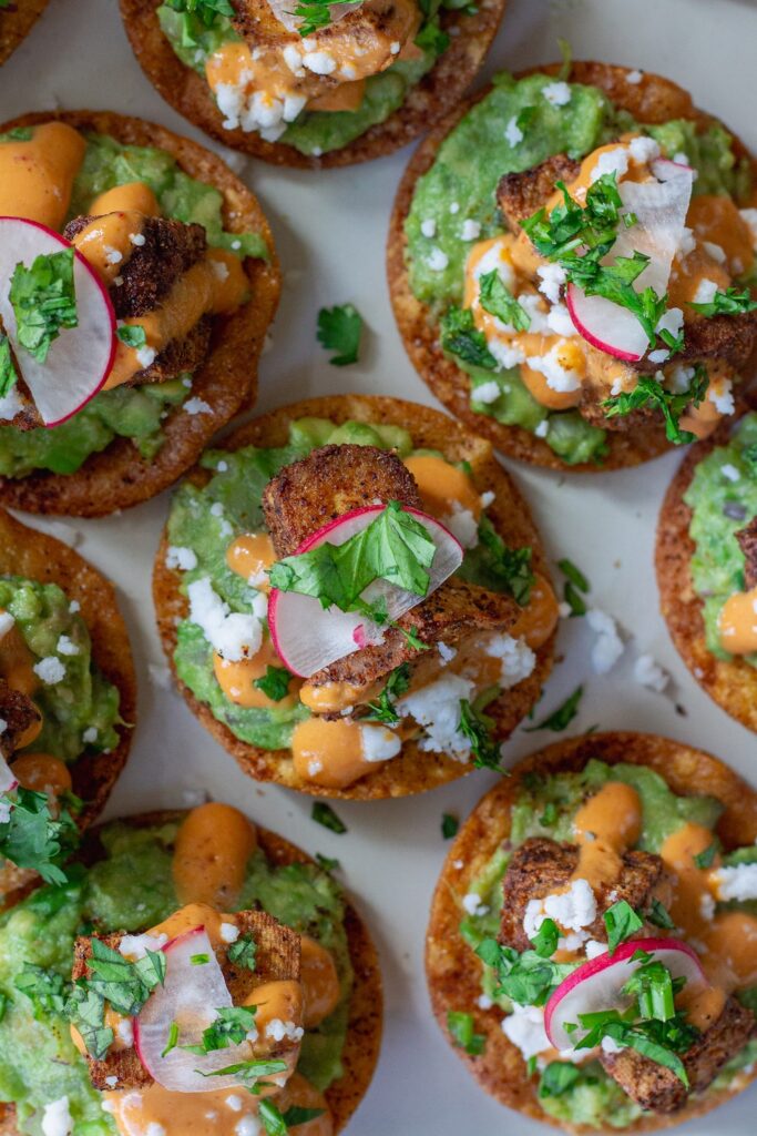 Bite-sized vegan tostadas with guacamole, crispy tofu, chipotle sour cream, and cilantro garnish