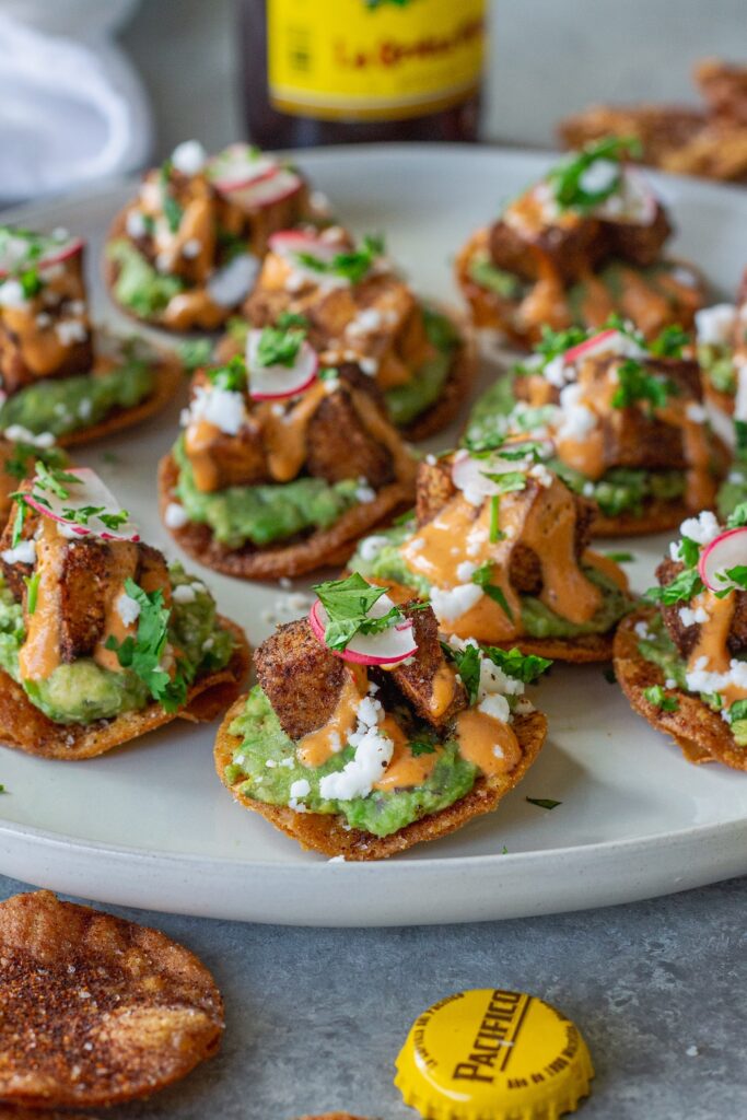 Bite-sized vegan tostadas with guacamole, crispy tofu, chipotle sour cream, and cilantro garnish
