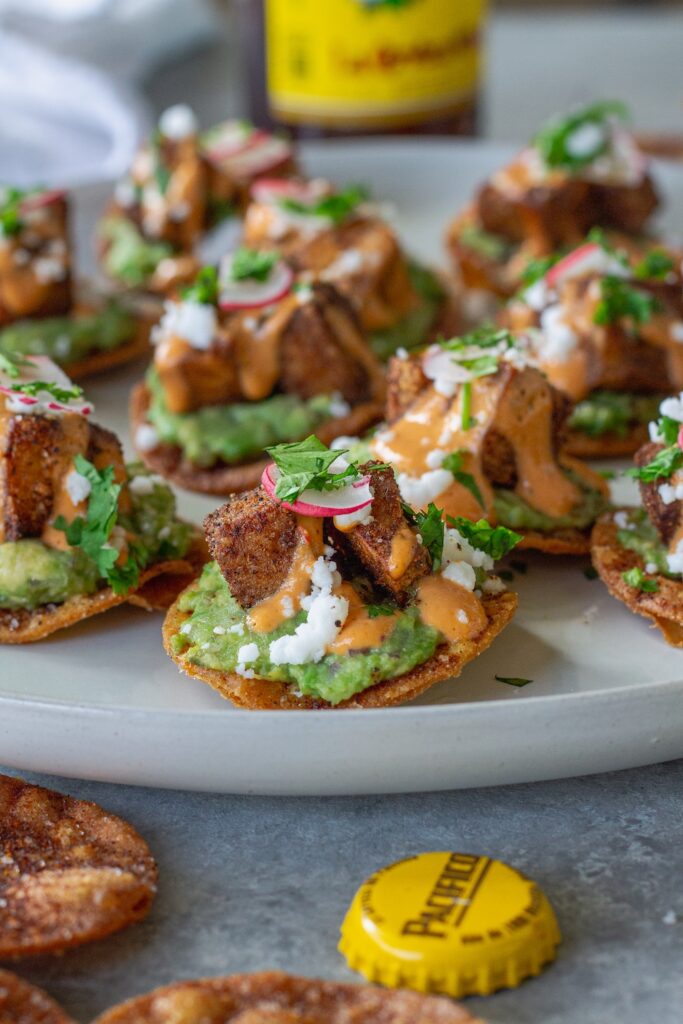 Bite-sized vegan tostadas with guacamole, crispy tofu, chipotle sour cream, and cilantro garnish