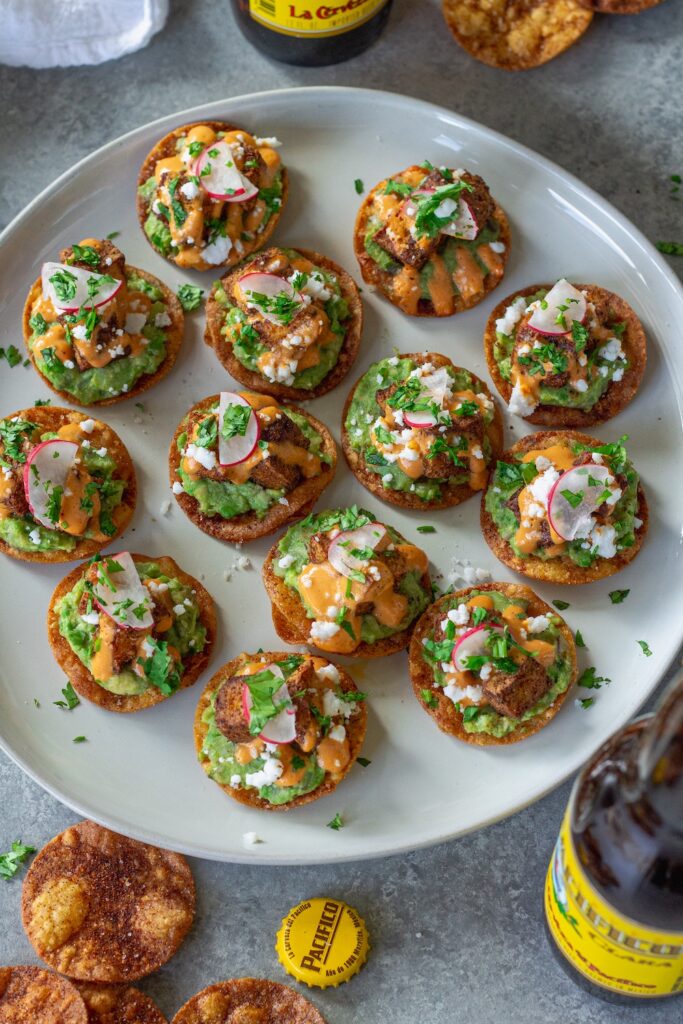 Bite-sized vegan tostadas with guacamole, crispy tofu, chipotle sour cream, and cilantro garnish